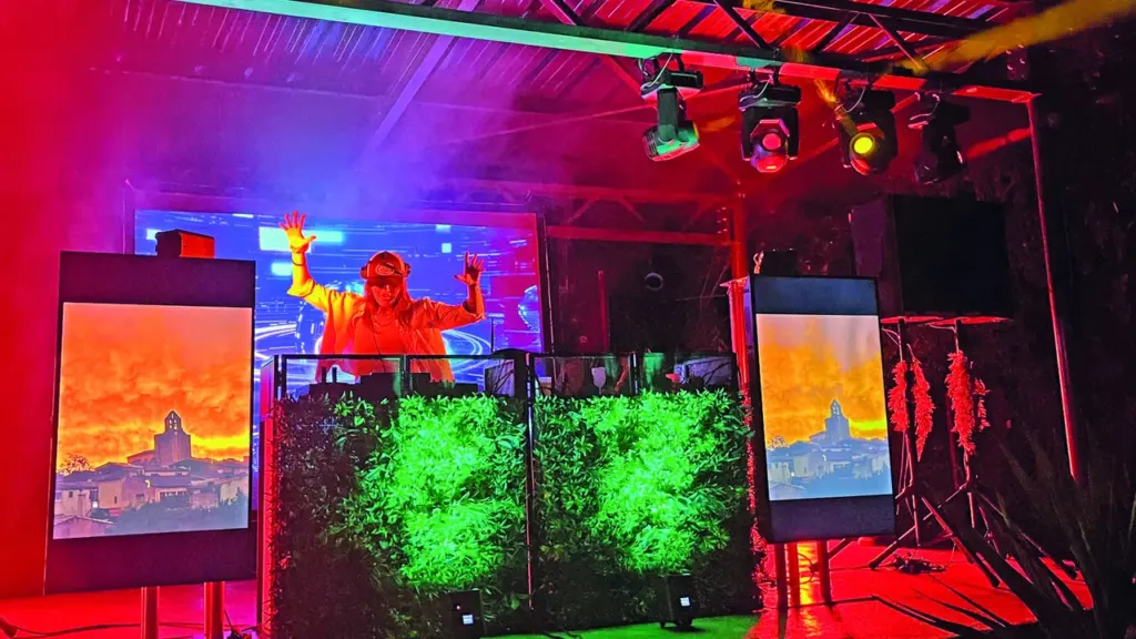 Un DJ portant une casquette mixe sur scène sous des éclairages rouges et verts vibrants.