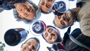 Cinq hommes souriants regardent vers le bas en tenant des verres de vin rouge.