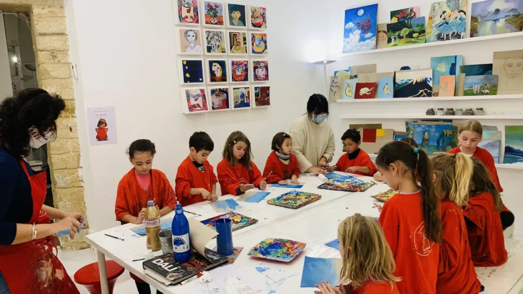 Un groupe d'enfants portant des tabliers rouges peignent autour d'une grande table dans l'atelier.