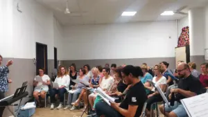 Une cheffe de chœur dirige une chorale composée de personnes assises tenant des partitions.