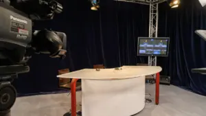 Un studio de télévision professionnel avec une caméra Panasonic, une table incurvée et divers projecteurs.
