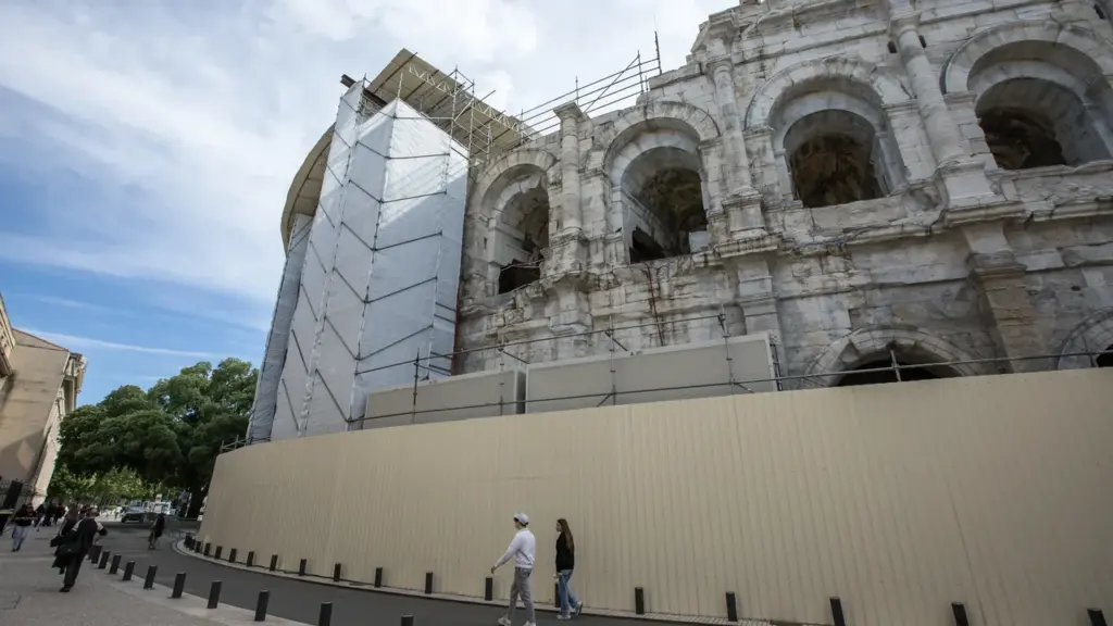 Deux personnes marchent devant les arènes de Nîmes en cours de rénovation avec échafaudages.
