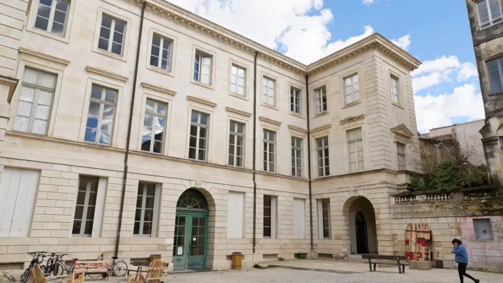 Une grande cour intérieure pavée devant une façade d'immeuble en pierre de style classique.
