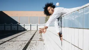 Un jeune homme aux cheveux bouclés, vêtu de blanc, joue avec une balle près d'une piscine.