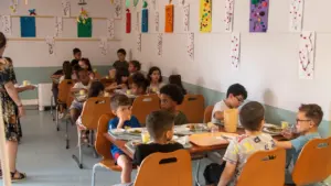 De nombreux enfants sont assis à des tables en bois pour prendre leur déjeuner scolaire.