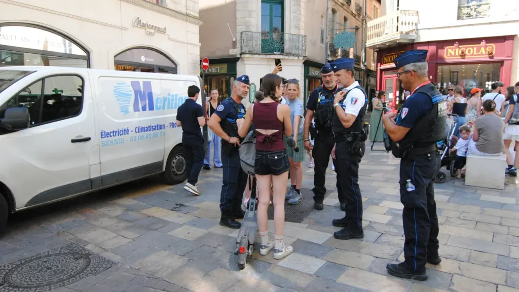 Trois policiers municipaux discutent avec une jeune femme sur une trottinette électrique en ville.