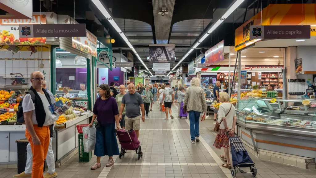 Allée intérieure animée des Halles de Nîmes avec des clients faisant leurs courses quotidiennes.