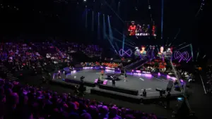 Deux joueurs de tennis de table s'échauffent sur une scène éclairée devant un large public.
