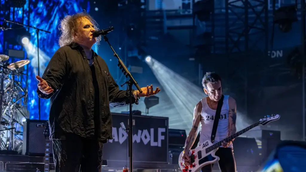 Robert Smith chante devant un micro sur scène avec un bassiste à ses côtés.