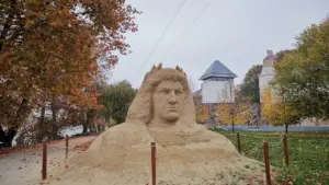 Une grande sculpture en sable représentant un visage historique dans un parc urbain français.